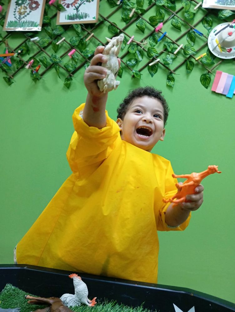 A boy laughing as he holds toy animals up in the air