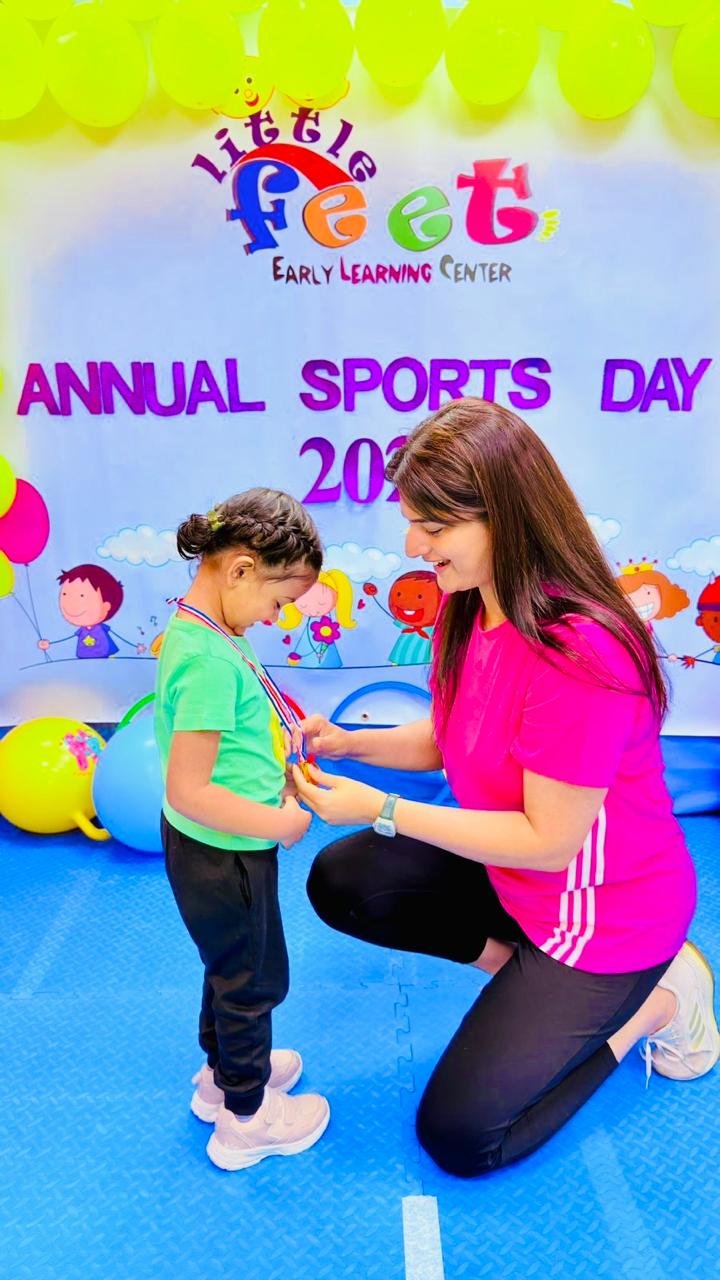 An educator kneeling to present a medal to a smiling girl on Sports Day